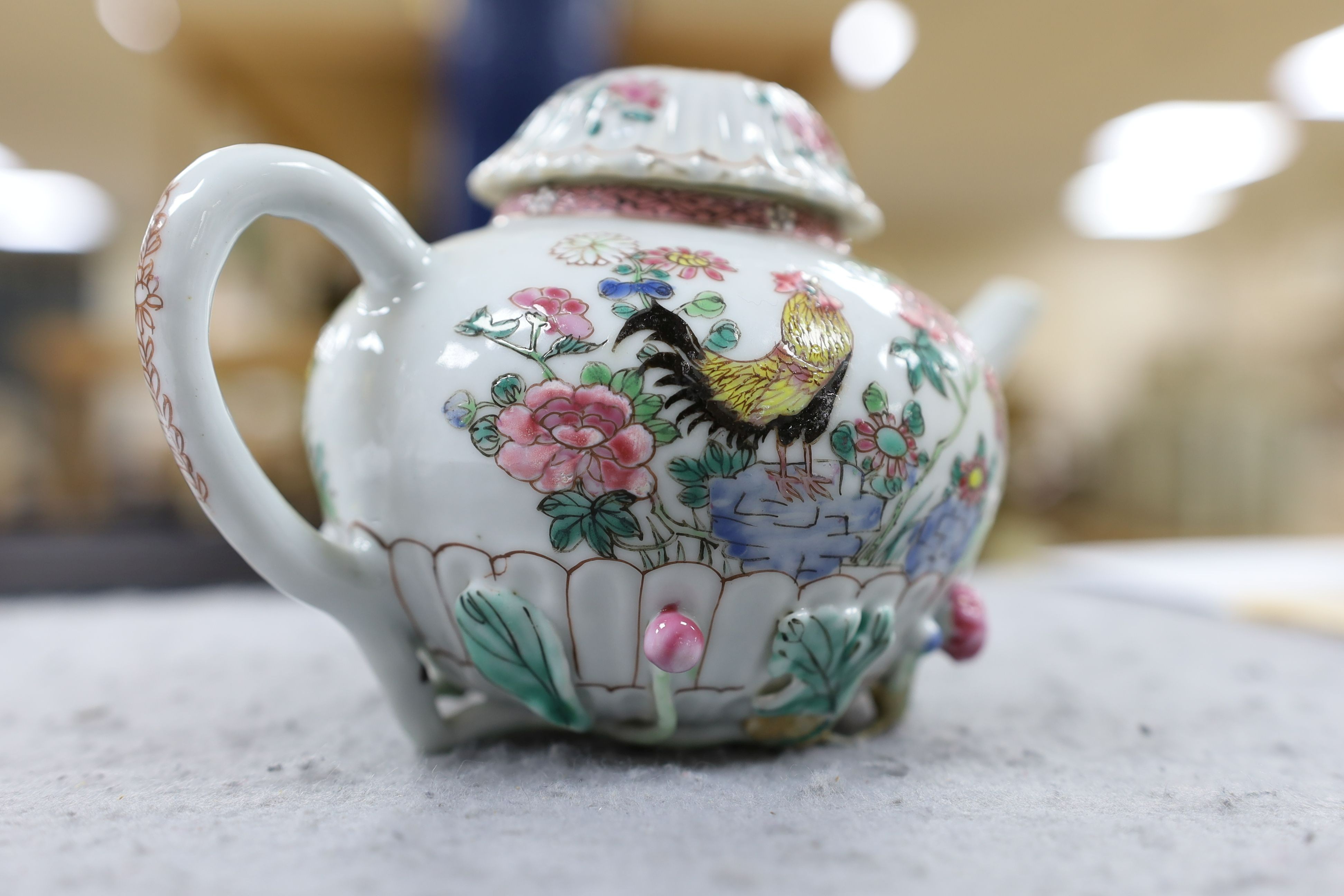 A Chinese famille rose chrysanthemum moulded teapot, early Qianlong period, painted with a cockerel amongst flowers, on a cage work base, 10 cms high